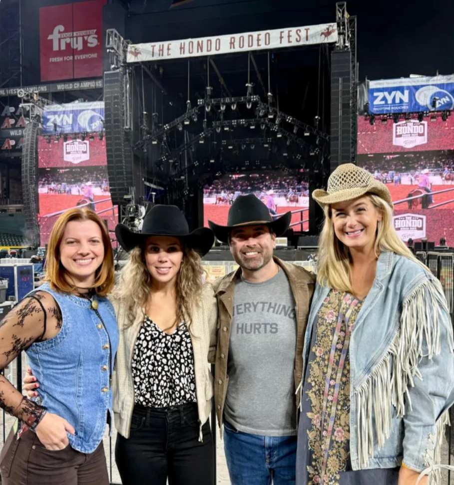 Four friends in western wear posing in front of the Hondo Rodeo Fest stage