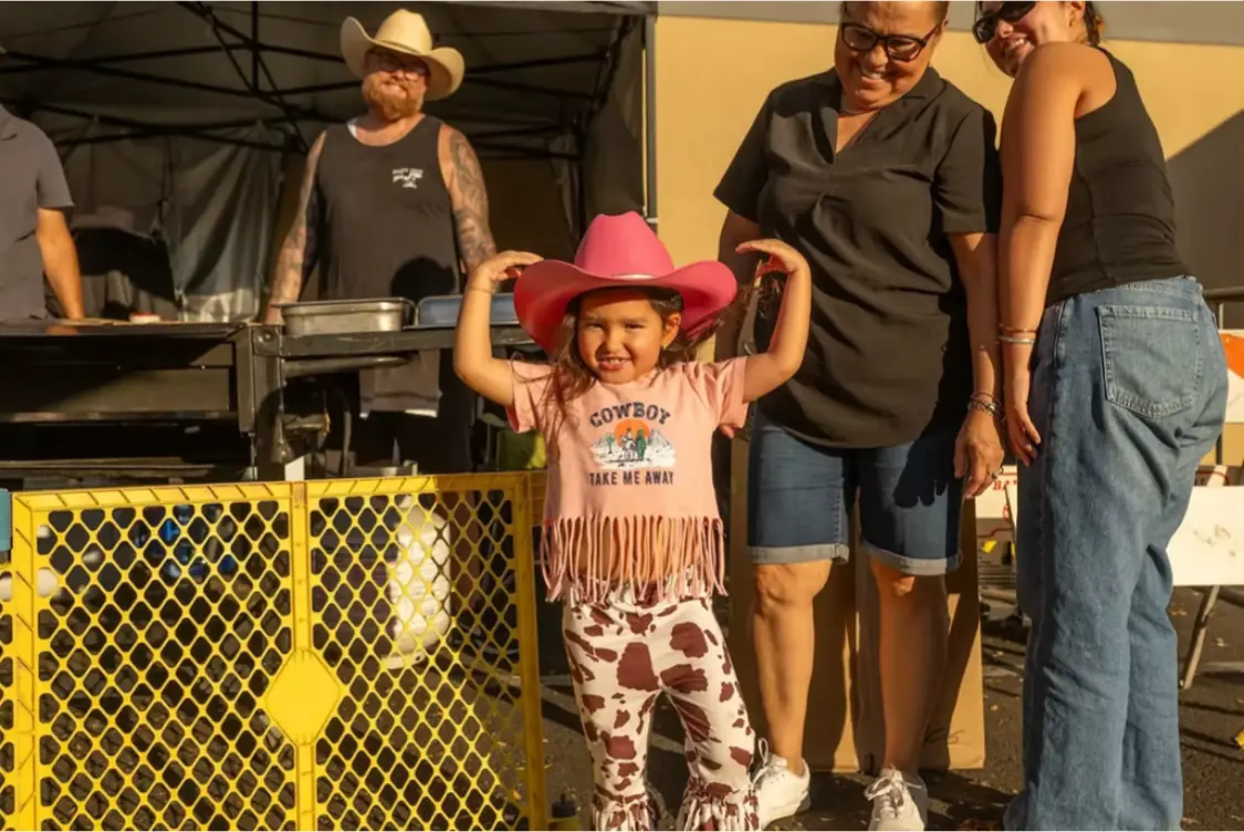 A child in a pink cowboy hat holding the brim
